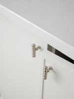 Two polished chrome beaded ball knobs mounted on white kitchen cabinet doors below countertop