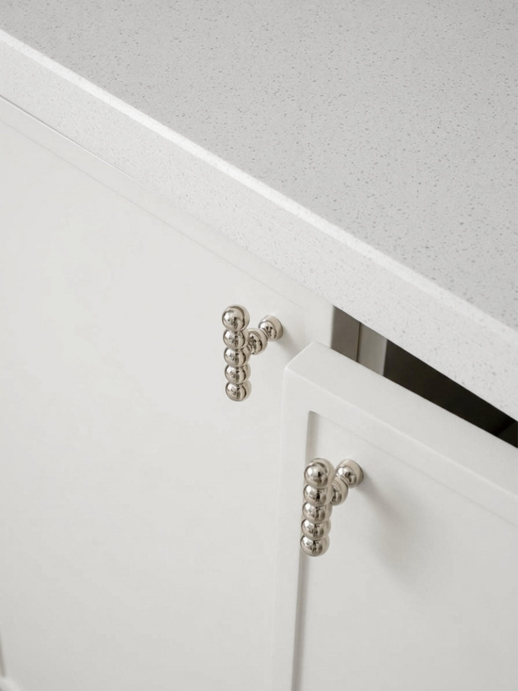 Two polished chrome beaded ball knobs mounted on white kitchen cabinet doors below countertop