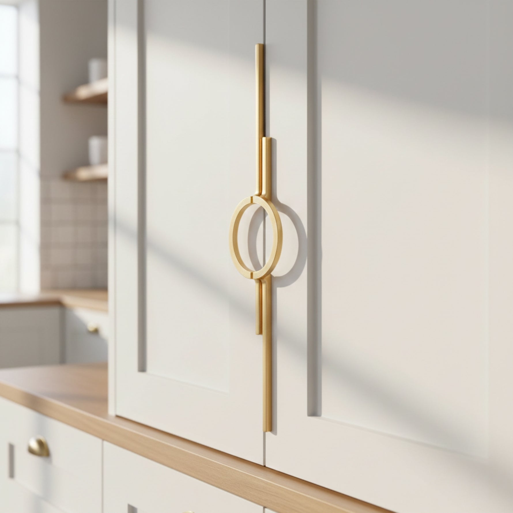 Satin gold circle ring cabinet pull on white shaker kitchen cabinet door, natural light