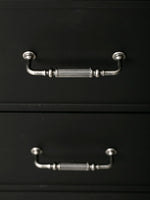 Two antique silver reeded pulls on black cabinet drawers, front view