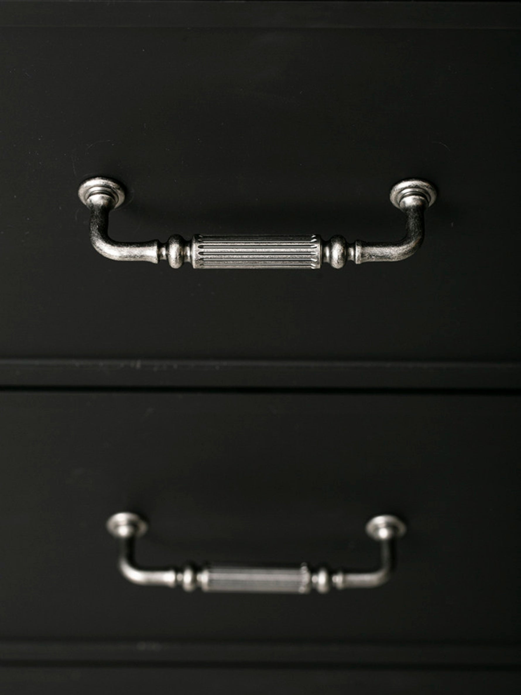 Two antique silver reeded pulls on black cabinet drawers, front view