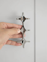 Hand holding a polished chrome star cross double pull against white cabinet door