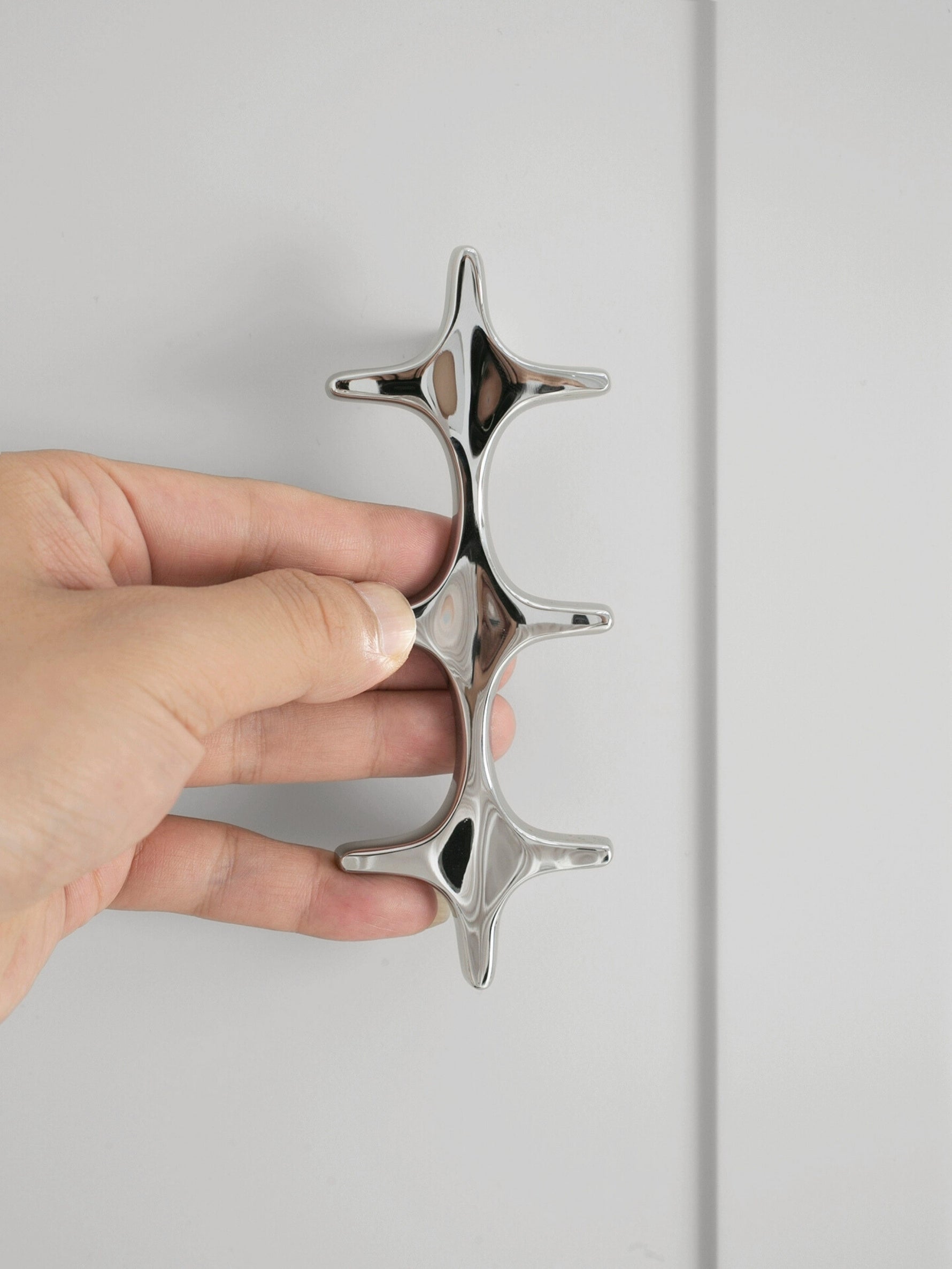 Hand holding a polished chrome star cross double pull against white cabinet door