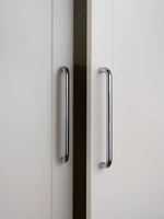 Two polished chrome bar cabinet pulls on white wardrobe doors, vertical