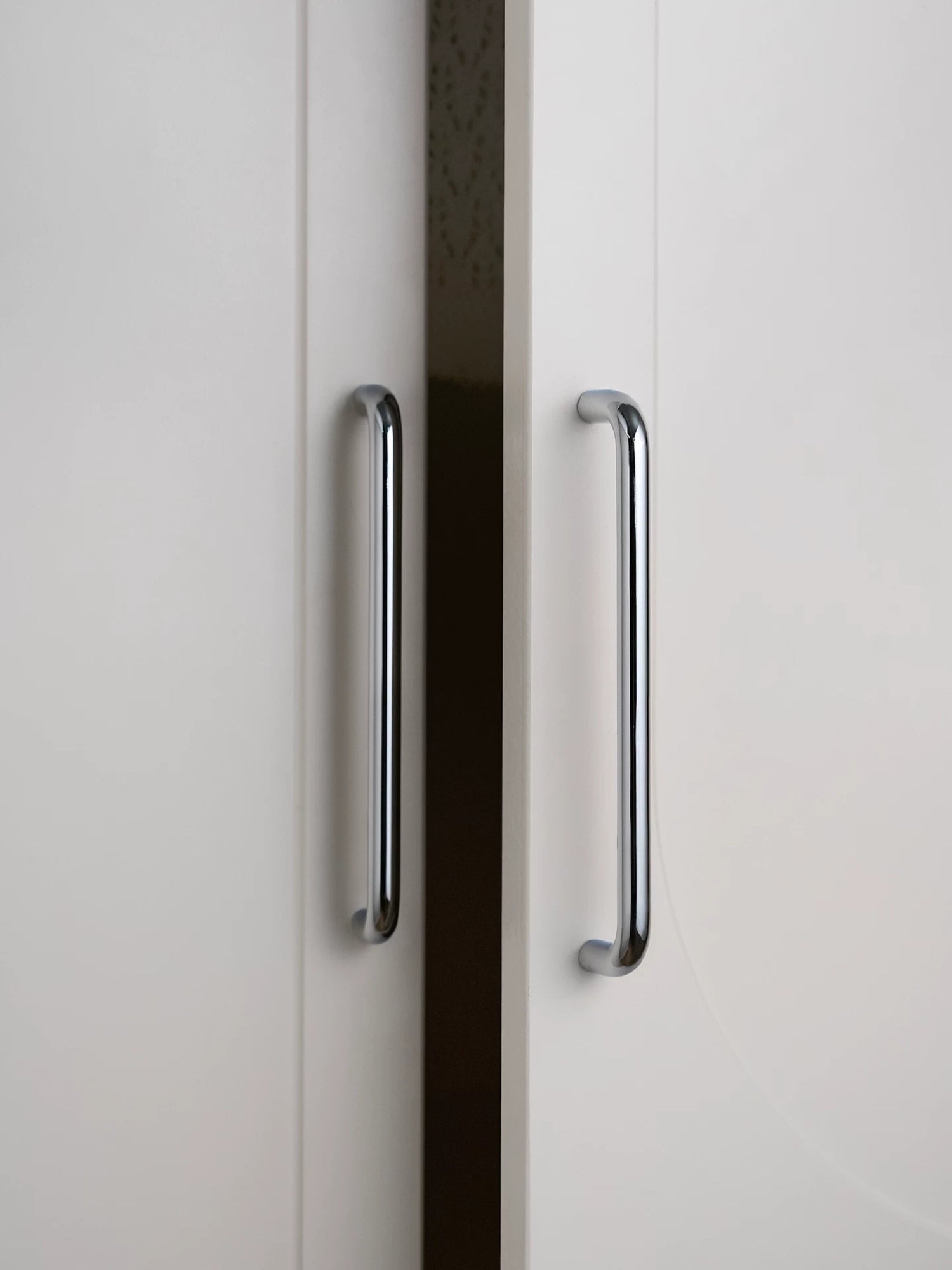 Two polished chrome bar cabinet pulls on white wardrobe doors, vertical