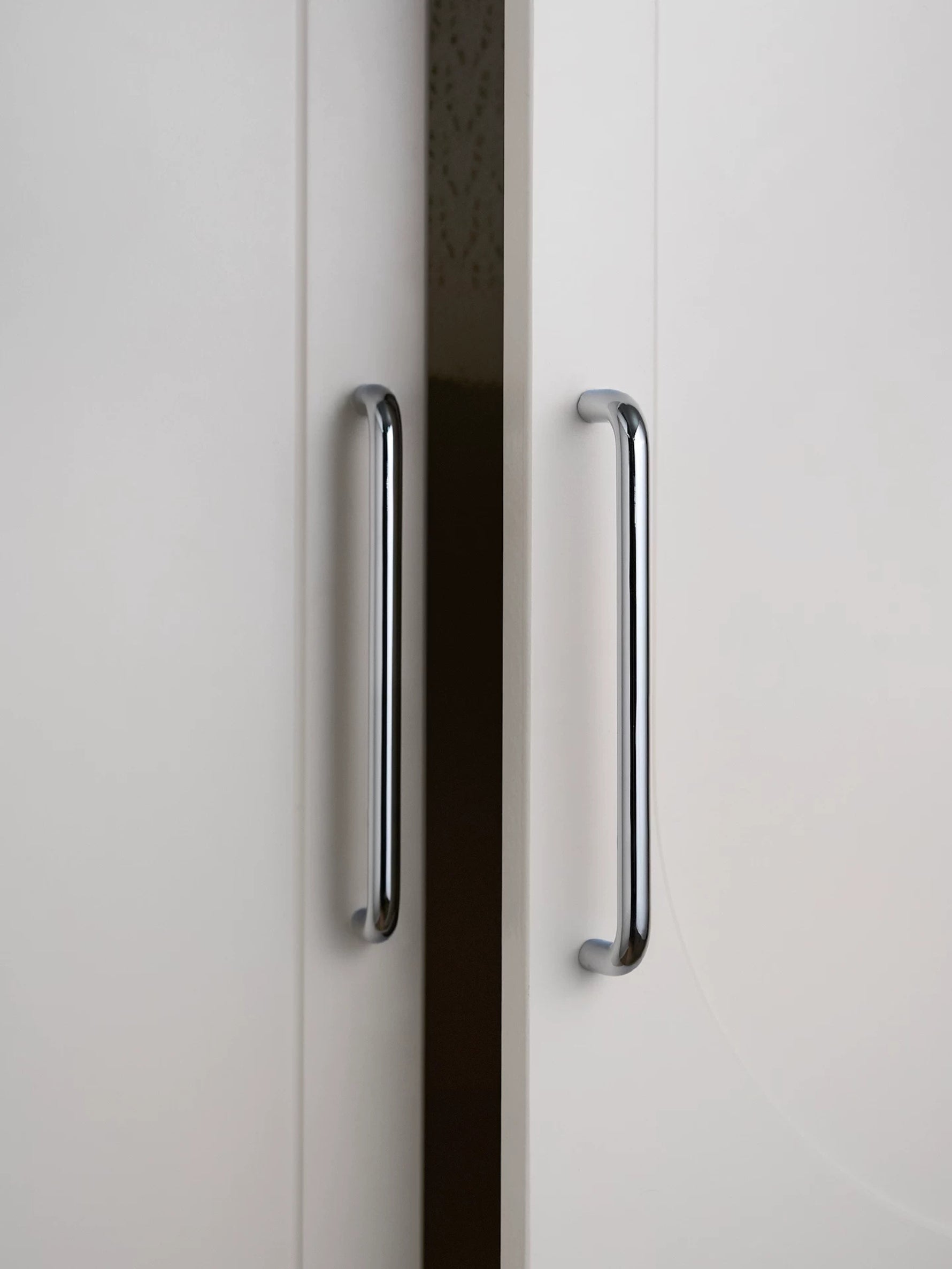 Two polished chrome bar cabinet pulls on white wardrobe doors, vertical