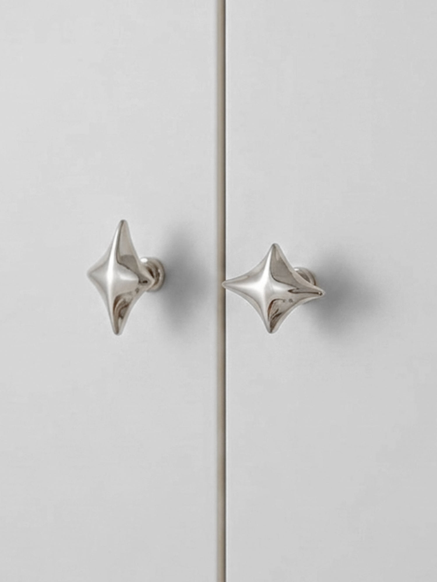 Two polished chrome star cabinet knobs on grey wardrobe doors, front view