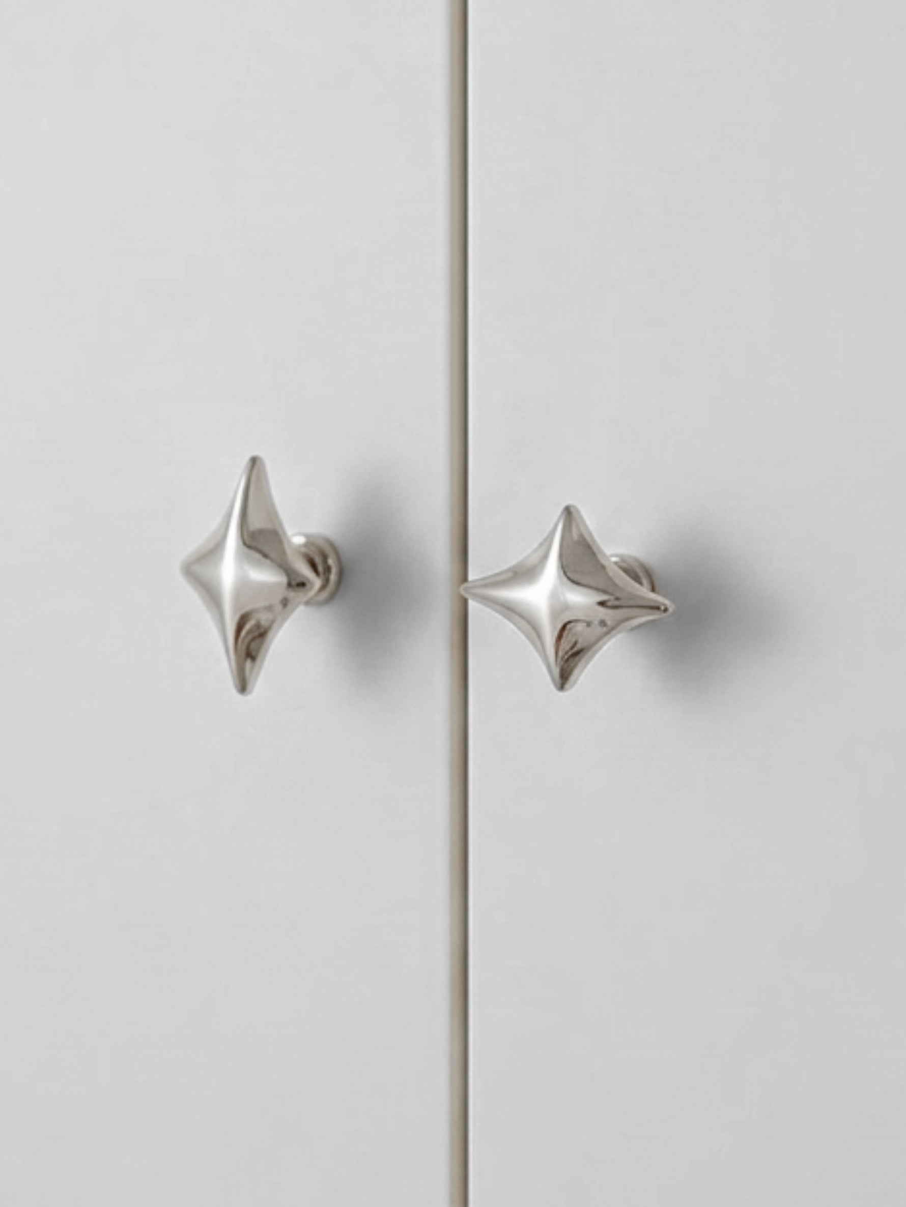 Two polished chrome star cabinet knobs on grey wardrobe doors, front view