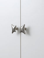 Polished chrome wave star cabinet knobs on white wardrobe door, front view