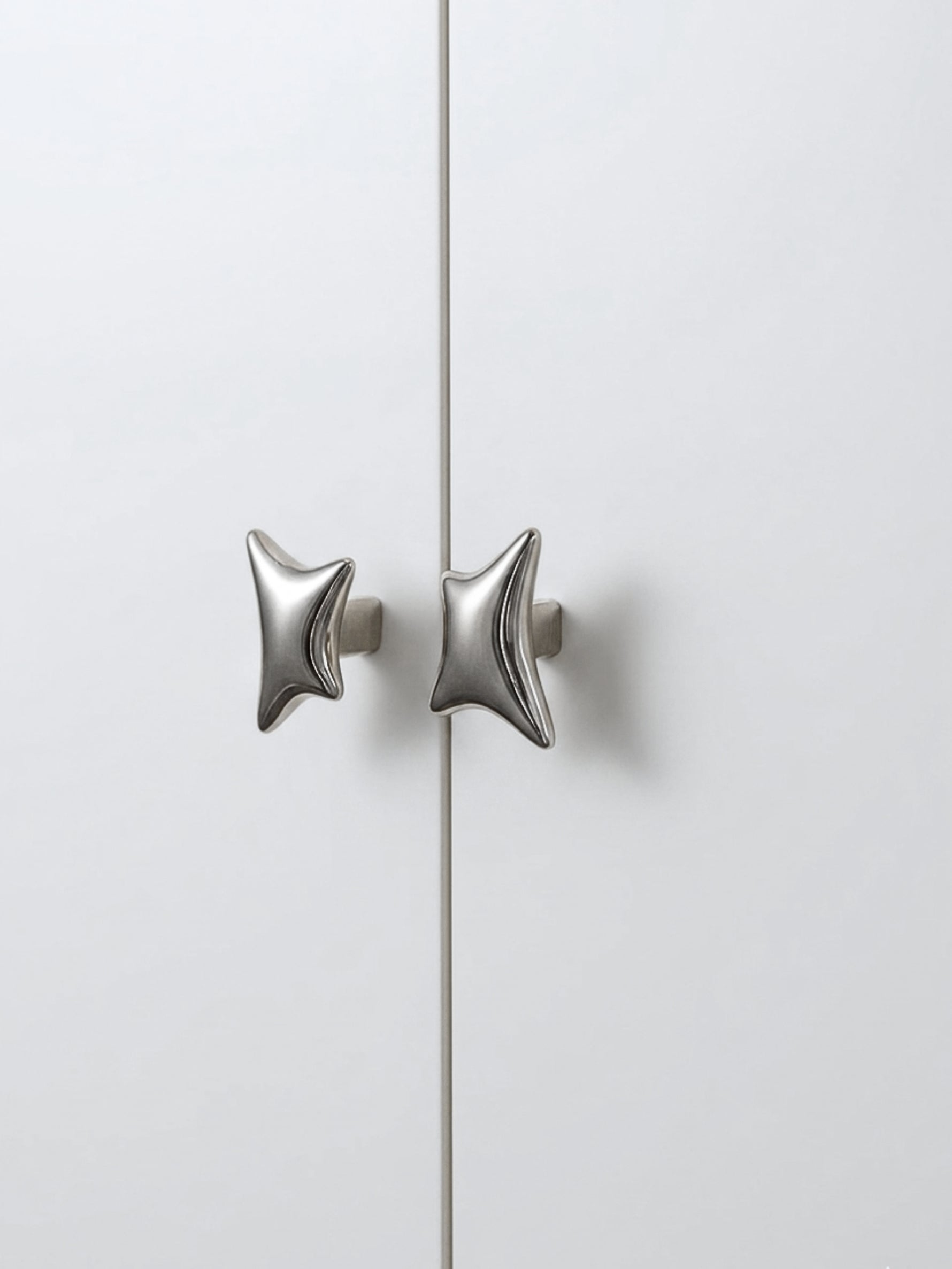 Polished chrome wave star cabinet knobs on white wardrobe door, front view