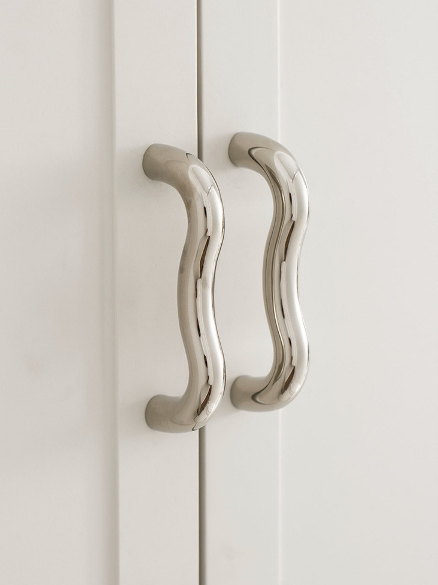 Two polished chrome wavy S-curve cabinet pulls on white wardrobe doors