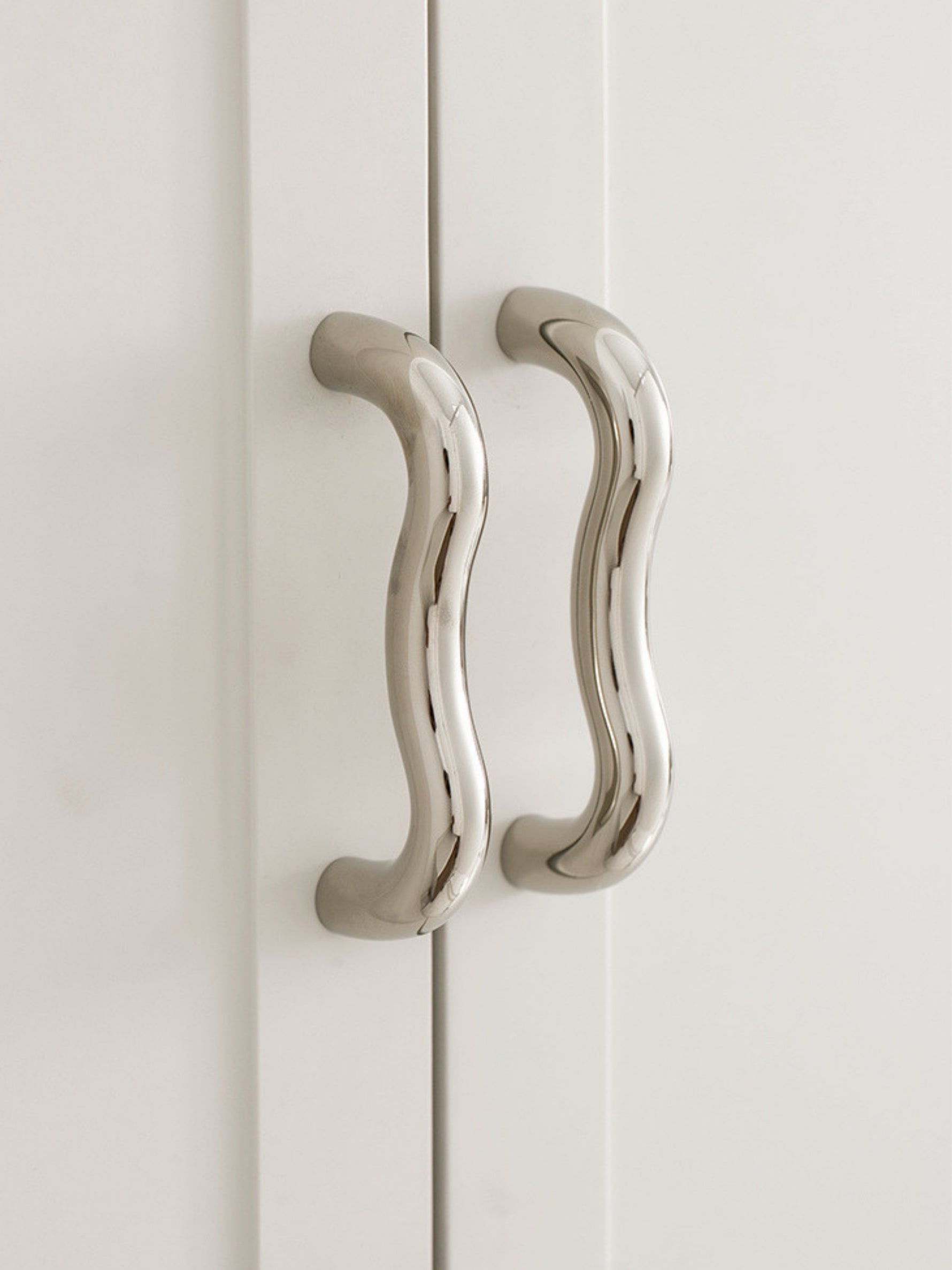 Two polished chrome wavy S-curve cabinet pulls on white wardrobe doors
