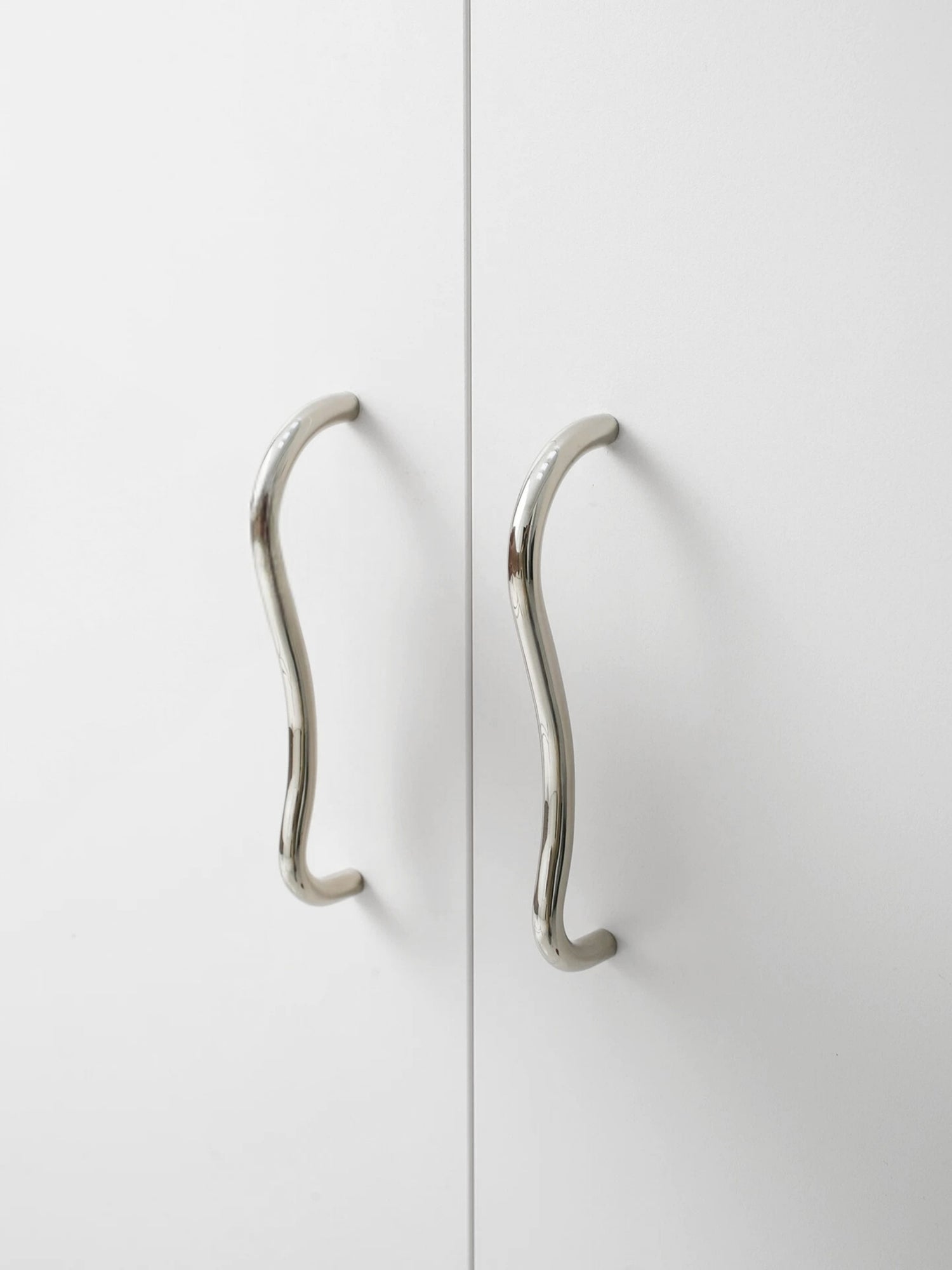 Chrome wave cabinet pull installed on white wardrobe doors