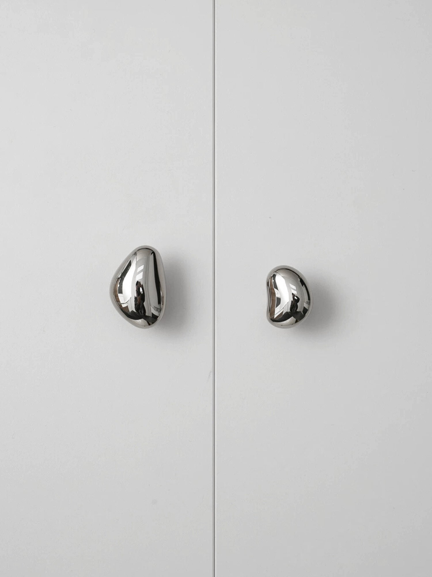 Two polished chrome pebble cabinet knobs on white wardrobe doors, front view