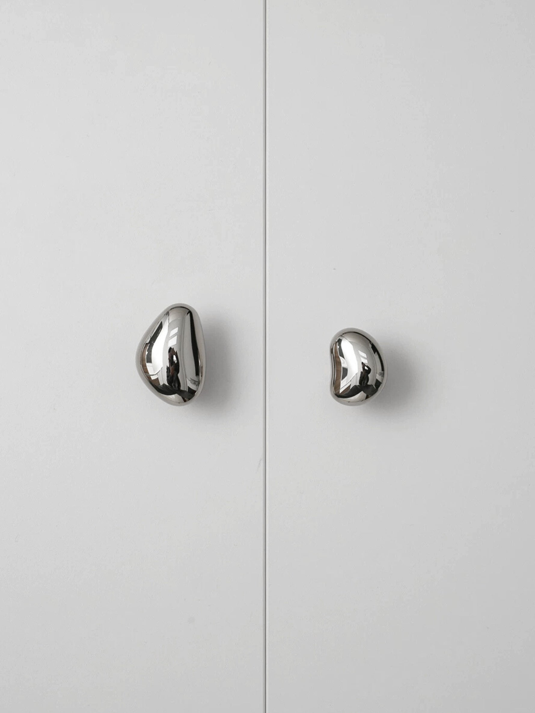 Two polished chrome pebble cabinet knobs on white wardrobe doors, front view
