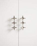 Two polished chrome star cross double pulls on white cabinet doors, front view
