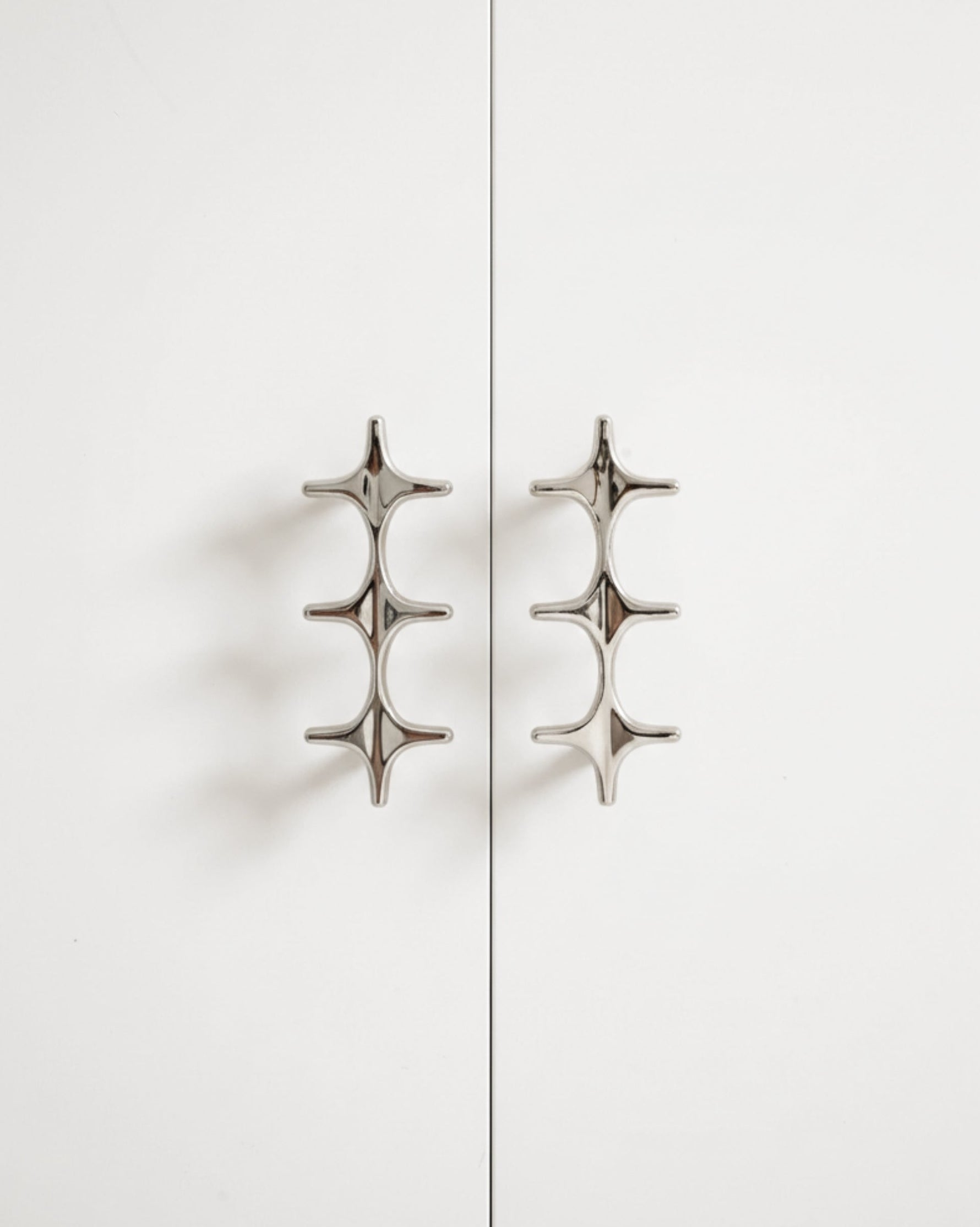Two polished chrome star cross double pulls on white cabinet doors, front view