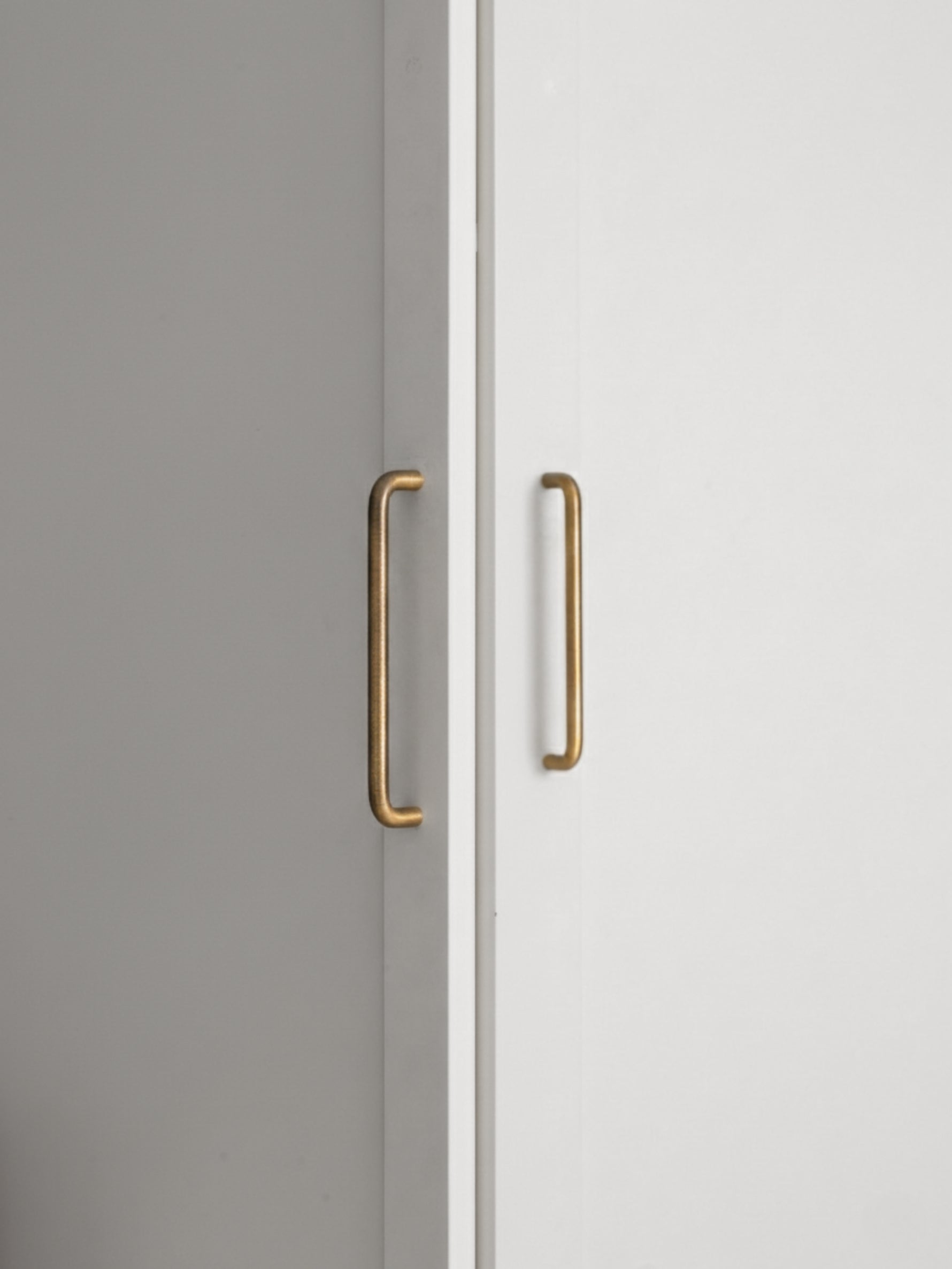 Two brushed brass handles on a white and gray cabinet