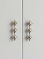 Two polished chrome star pulls on grey cabinet doors, front view