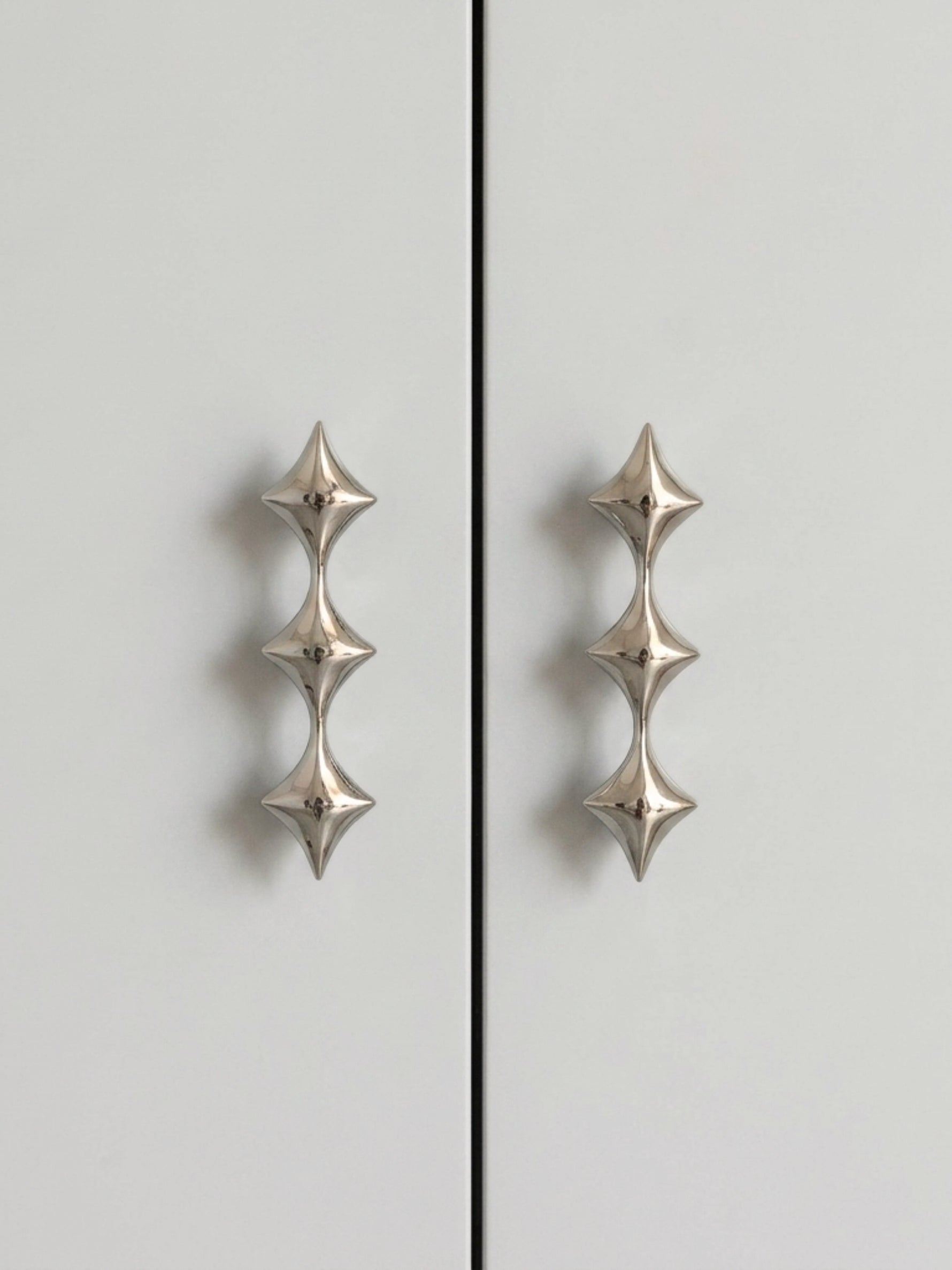 Two polished chrome star pulls on grey cabinet doors, front view