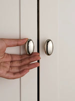 Hand holding nickel silver oval cabinet knob on white shaker cabinet door