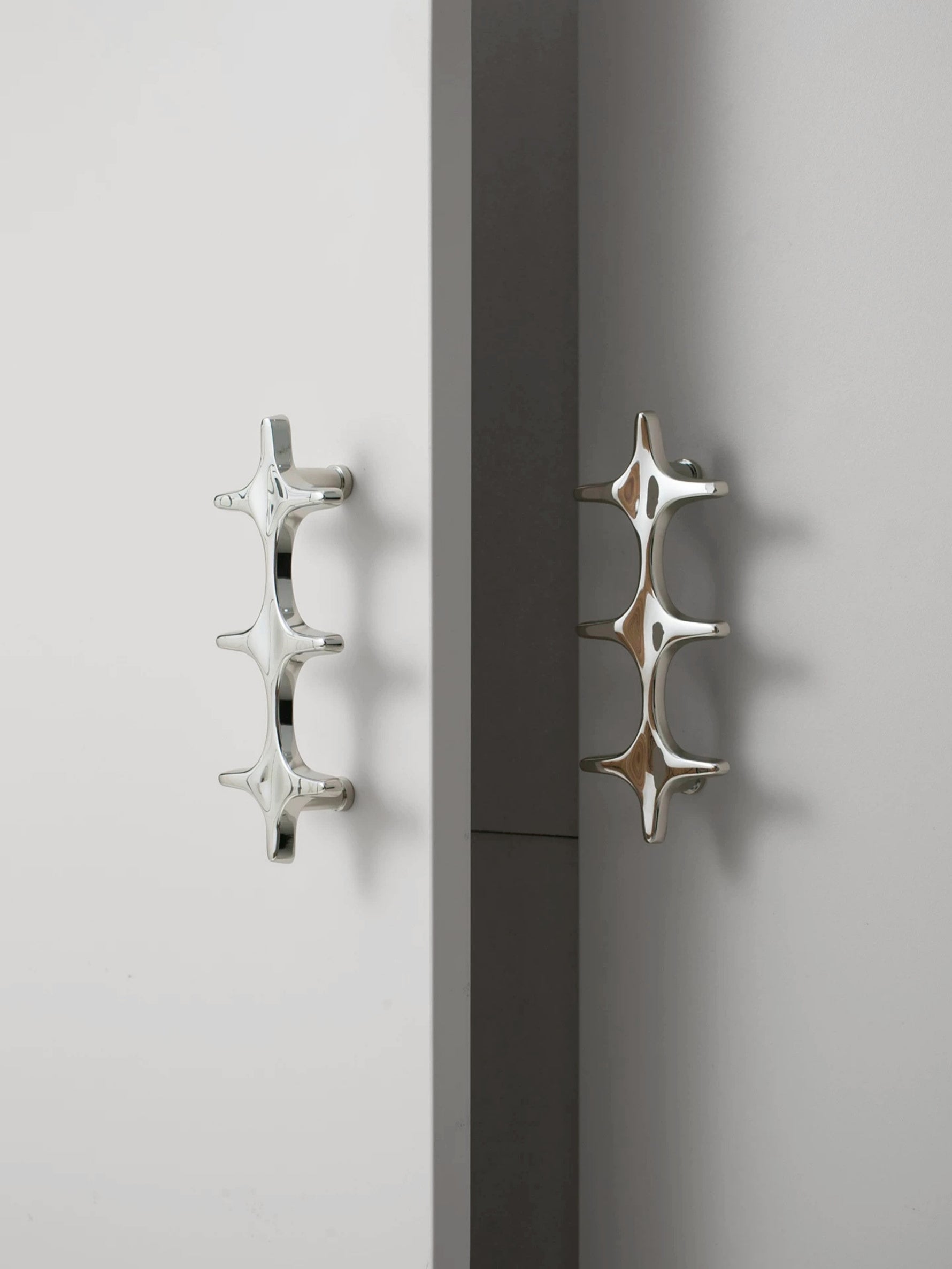 Two polished chrome star cross pulls on white cabinet doors, side angle showing depth
