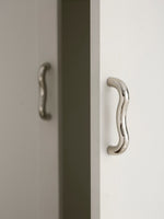 Single polished chrome wavy S-curve pull on white cabinet edge, side view