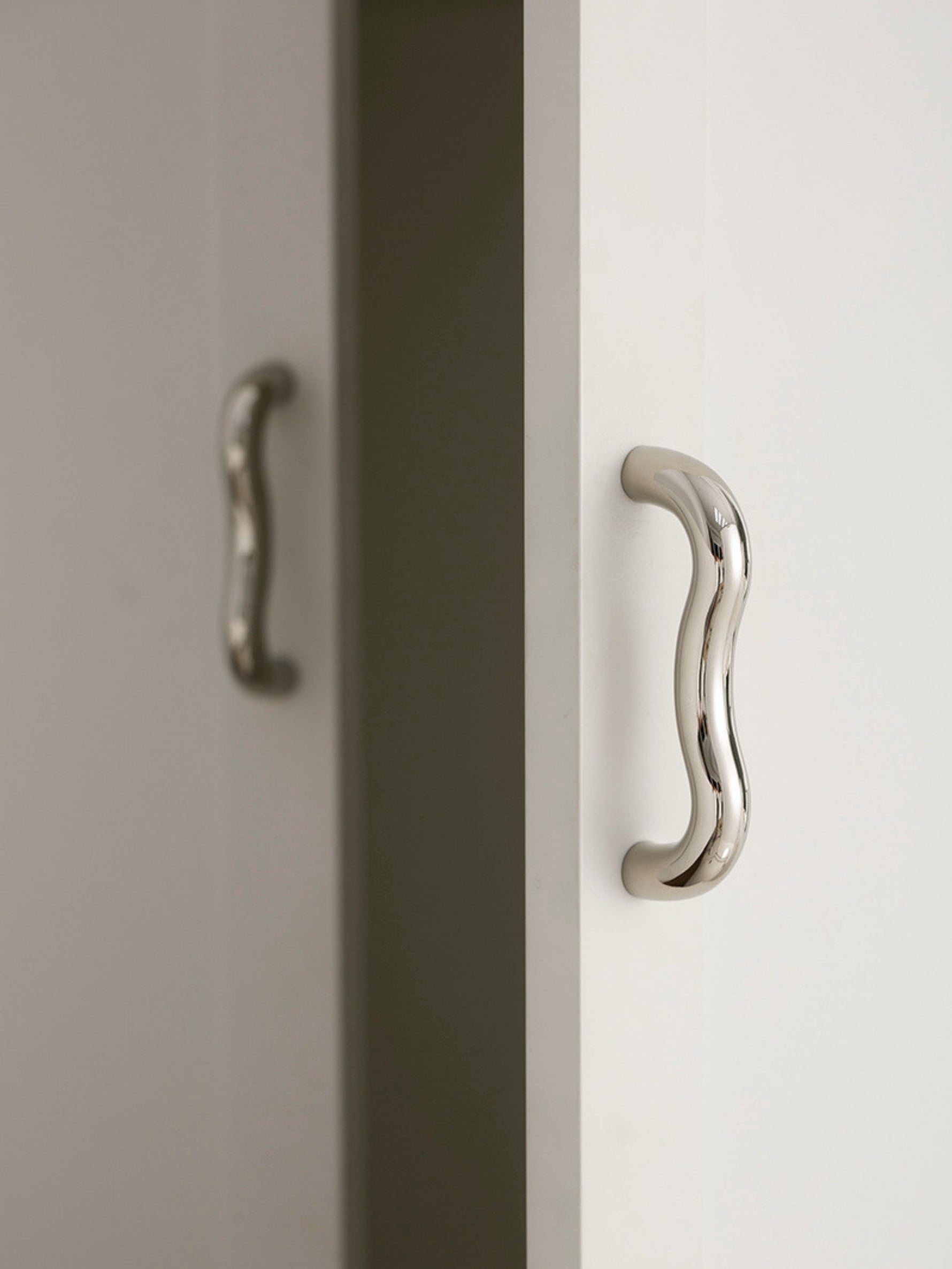 Single polished chrome wavy S-curve pull on white cabinet edge, side view