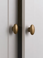 Two antique brass oval knobs on white Shaker cabinet doors