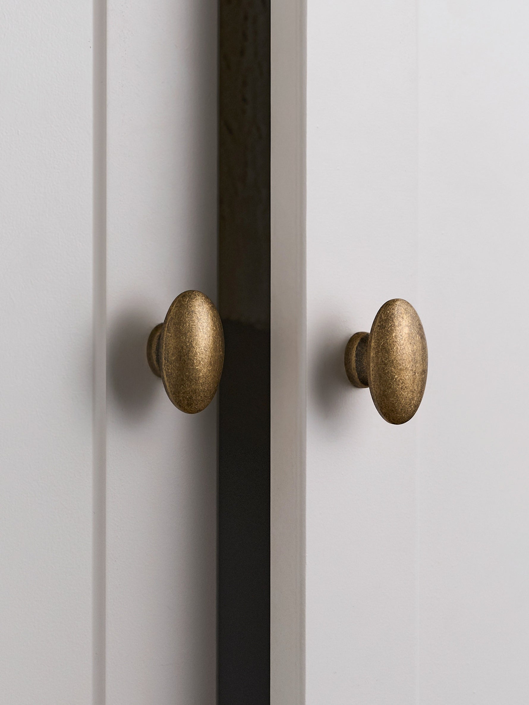 Two antique brass oval knobs on white Shaker cabinet doors