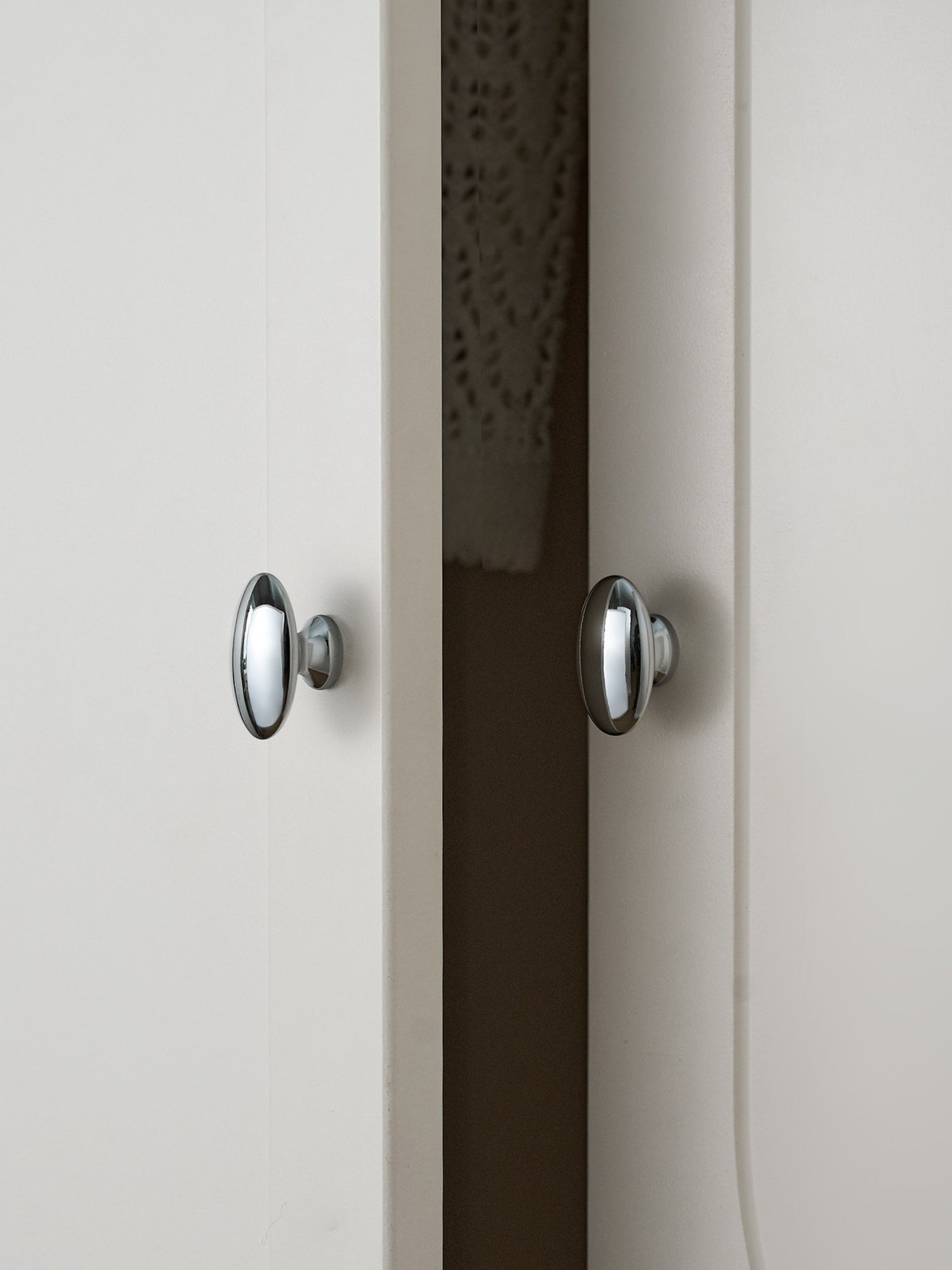 Two polished chrome oval knobs on white and dark cabinet doors
