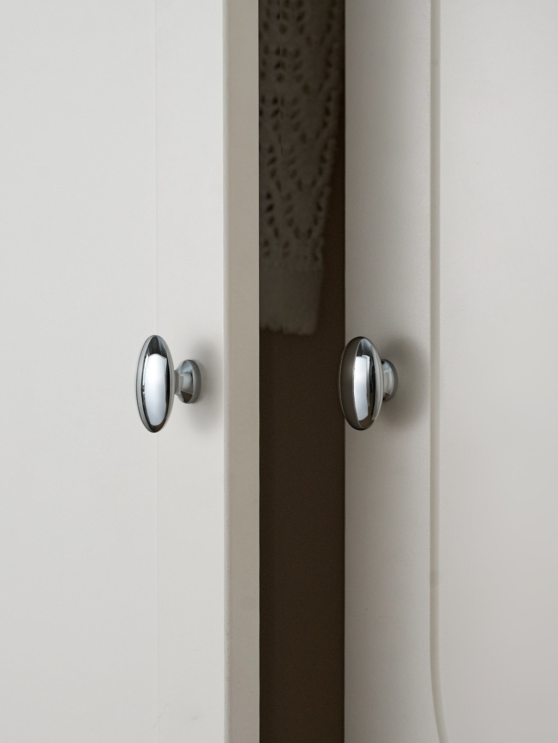 Two polished chrome oval knobs on white and dark cabinet doors