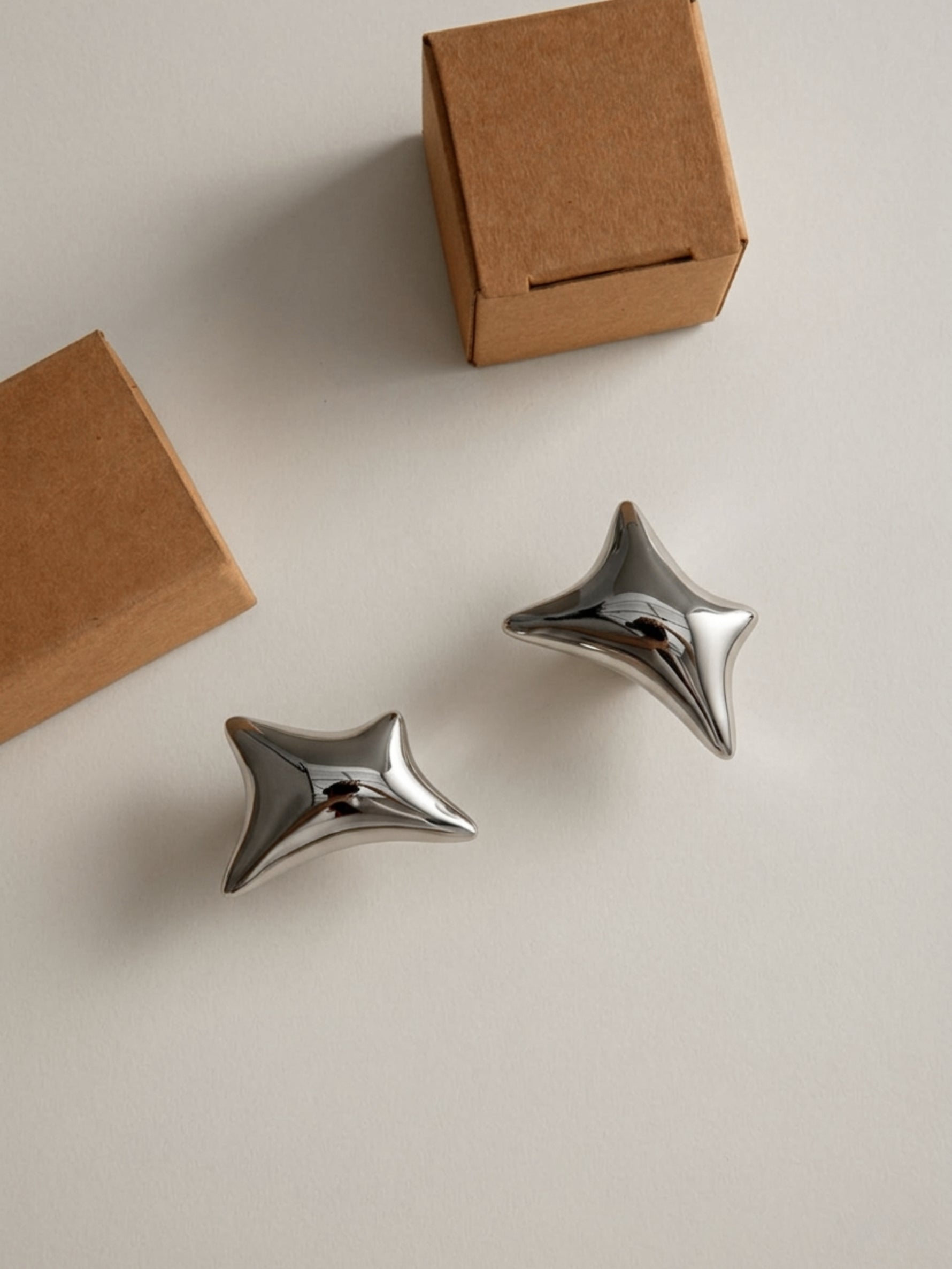 Two polished chrome wave star knobs and kraft gift boxes on beige surface, flat lay