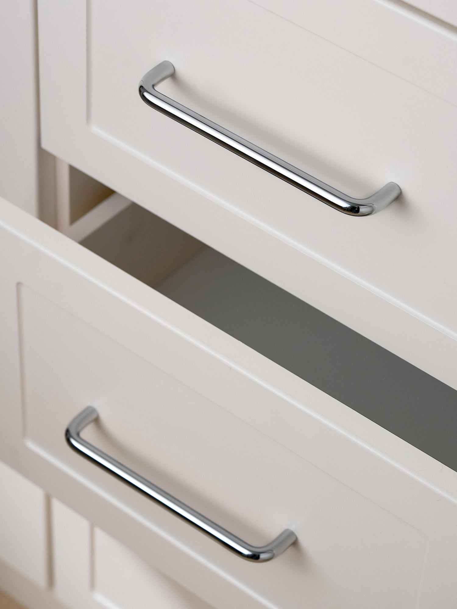 Polished chrome bar pulls on open cream Shaker drawer fronts