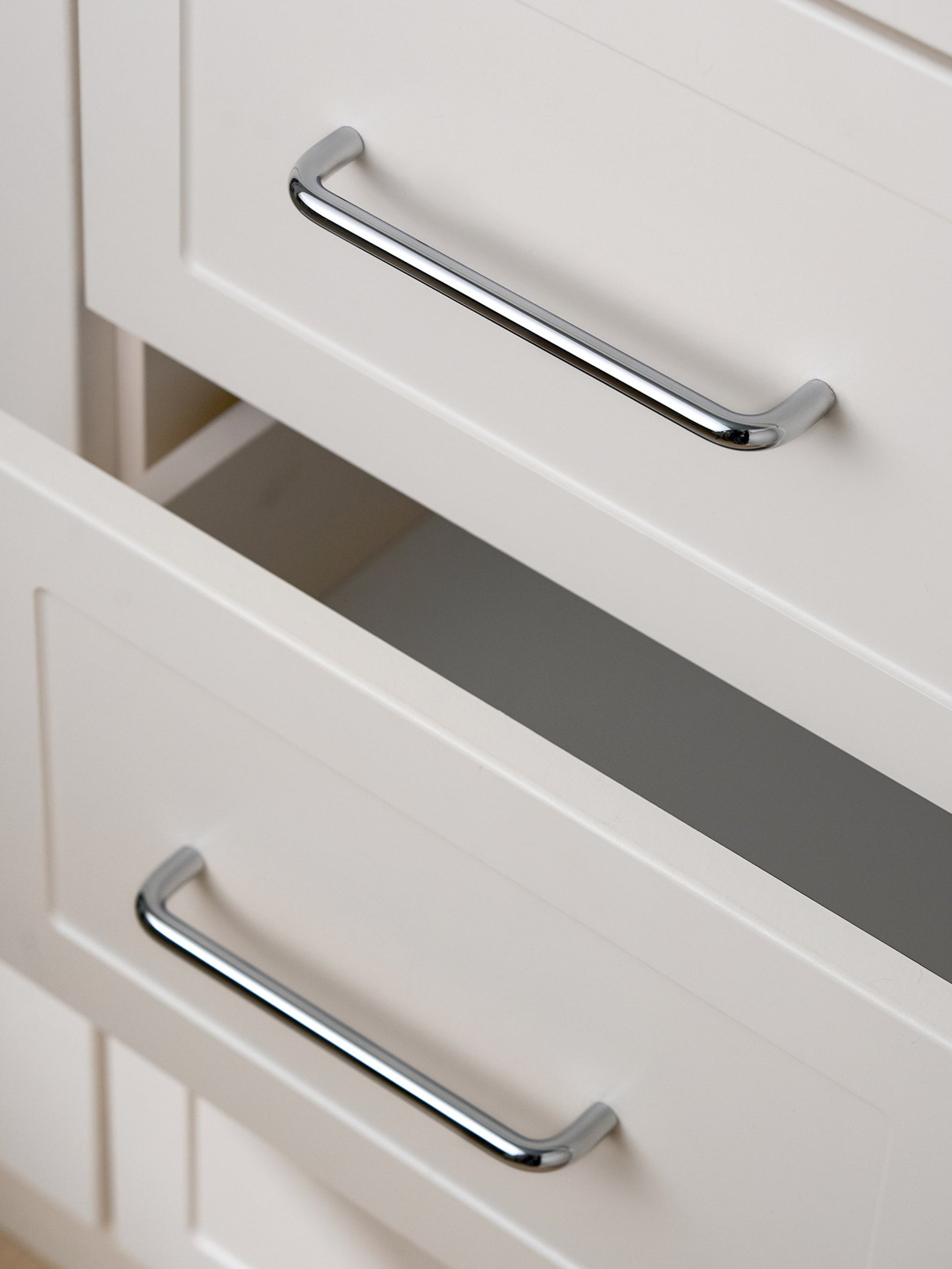 Polished chrome bar pulls on open cream Shaker drawer fronts