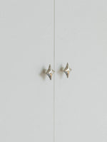 Two polished chrome star knobs on grey cabinet doors, distant view