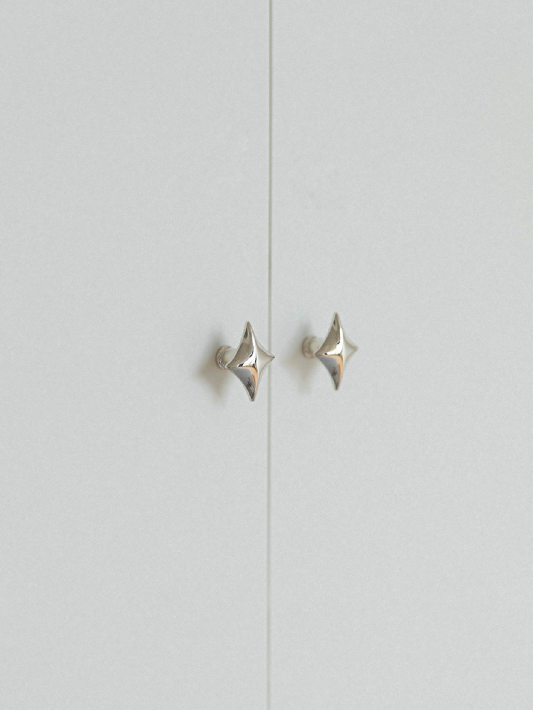 Two polished chrome star knobs on grey cabinet doors, distant view