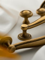 Close-up antique brass beaded knob and bar pull detail on white fabric