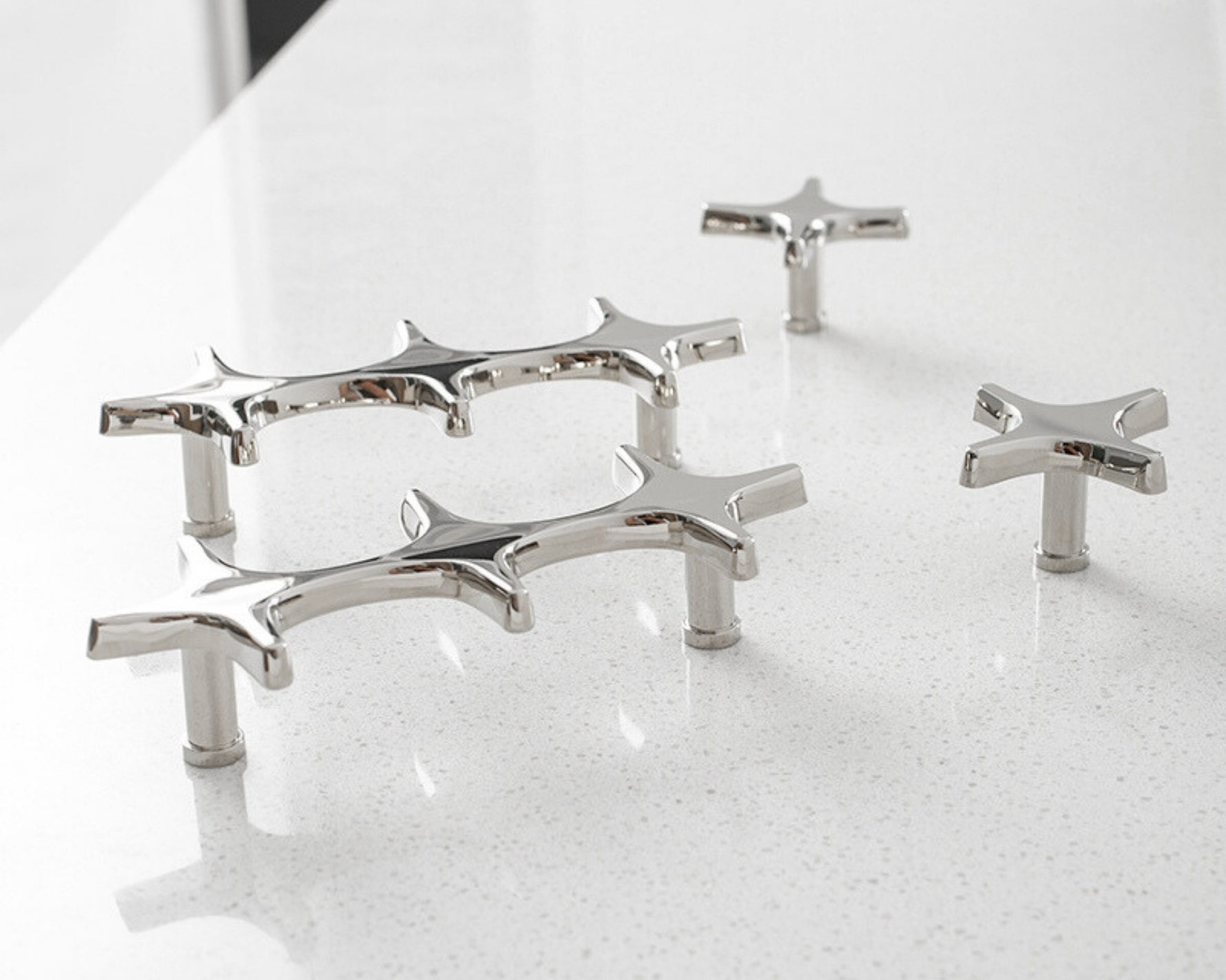 Five polished chrome star cross pulls and knobs arranged on white speckled countertop