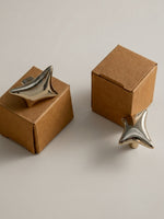 Polished chrome and gold wave star knobs balanced on kraft gift boxes, angled view