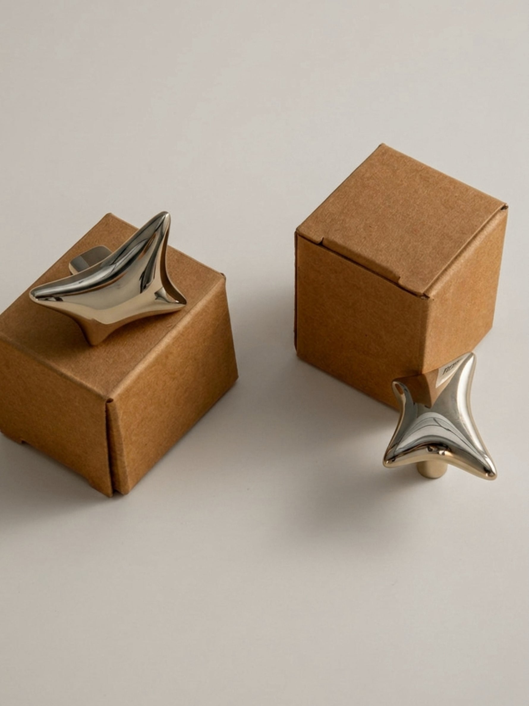 Polished chrome and gold wave star knobs balanced on kraft gift boxes, angled view