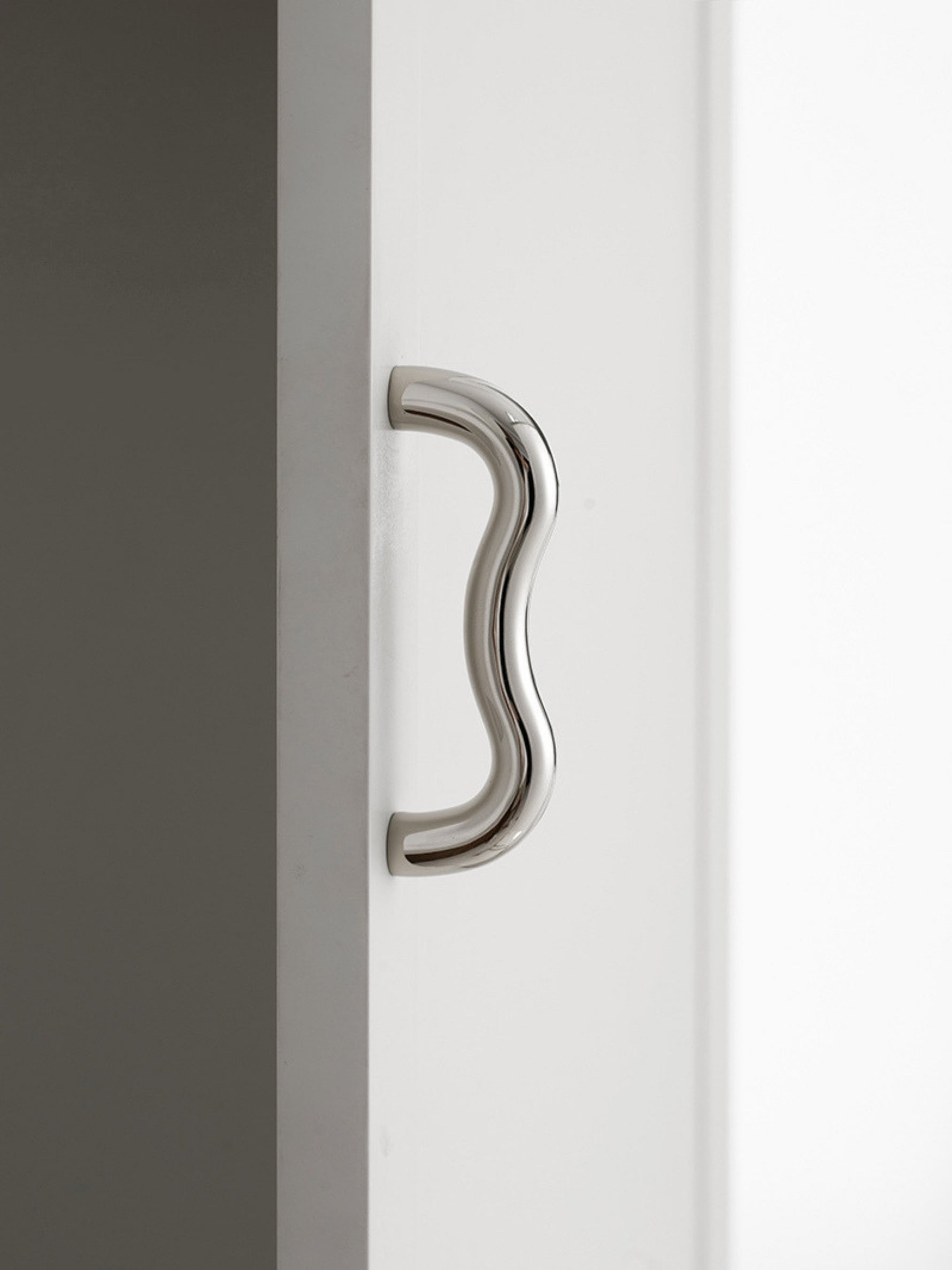 Close-up polished chrome wavy S-curve pull mounted vertically on white cabinet door