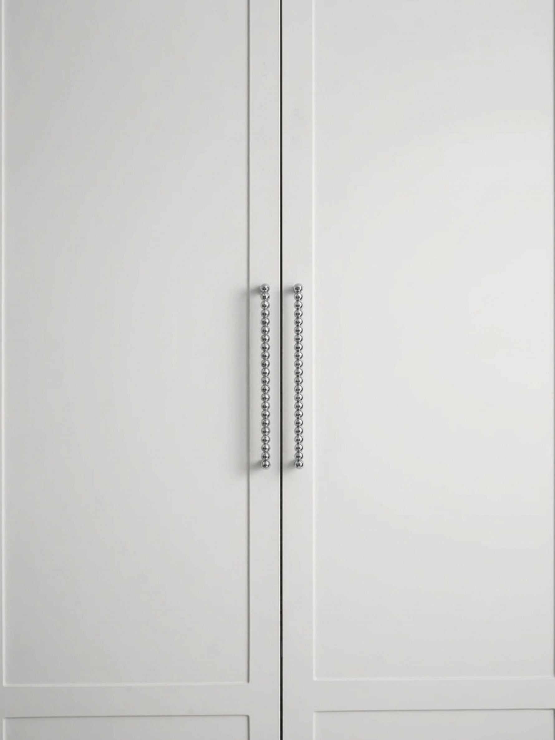 Two polished chrome beaded ball pulls on white shaker cabinet doors, front view