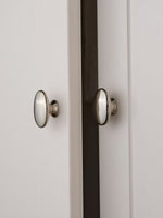 Two nickel silver oval knobs installed on white shaker cabinet doors