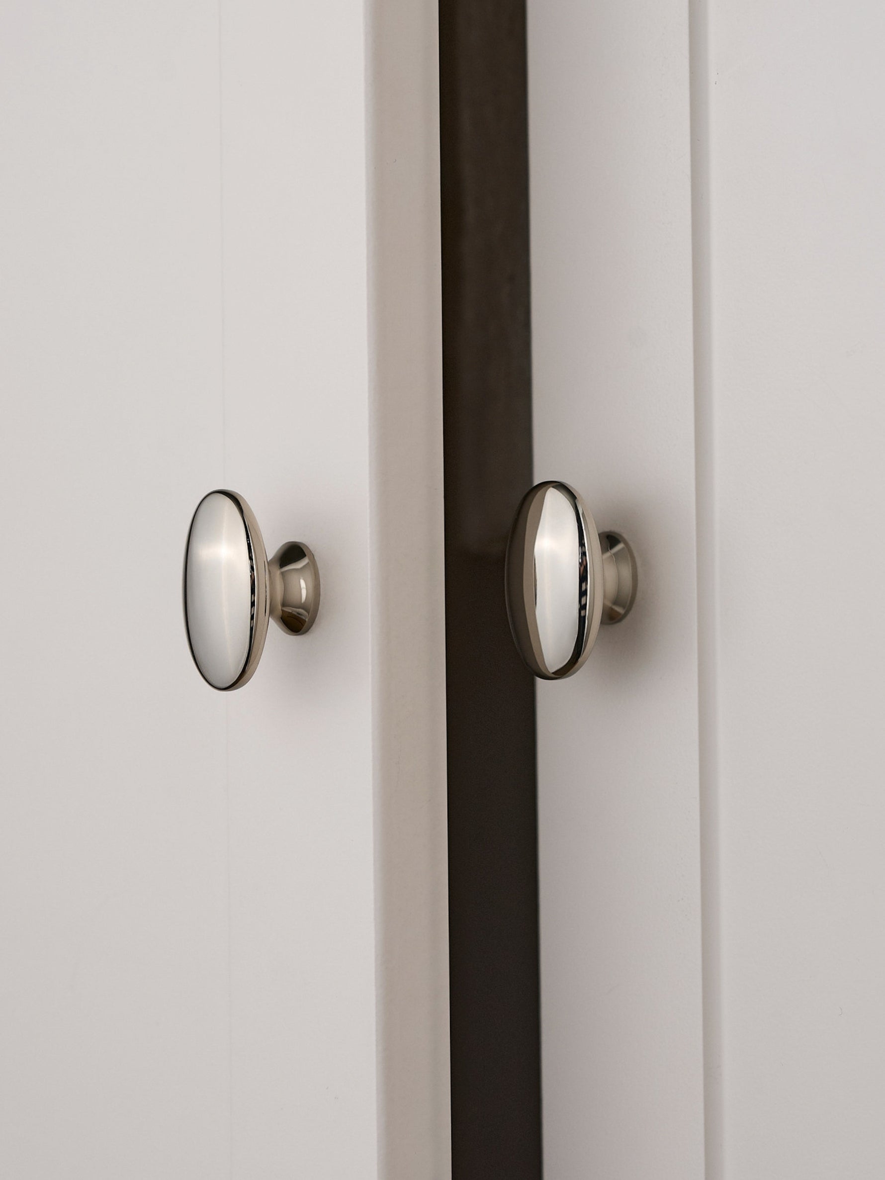Two nickel silver oval knobs installed on white shaker cabinet doors