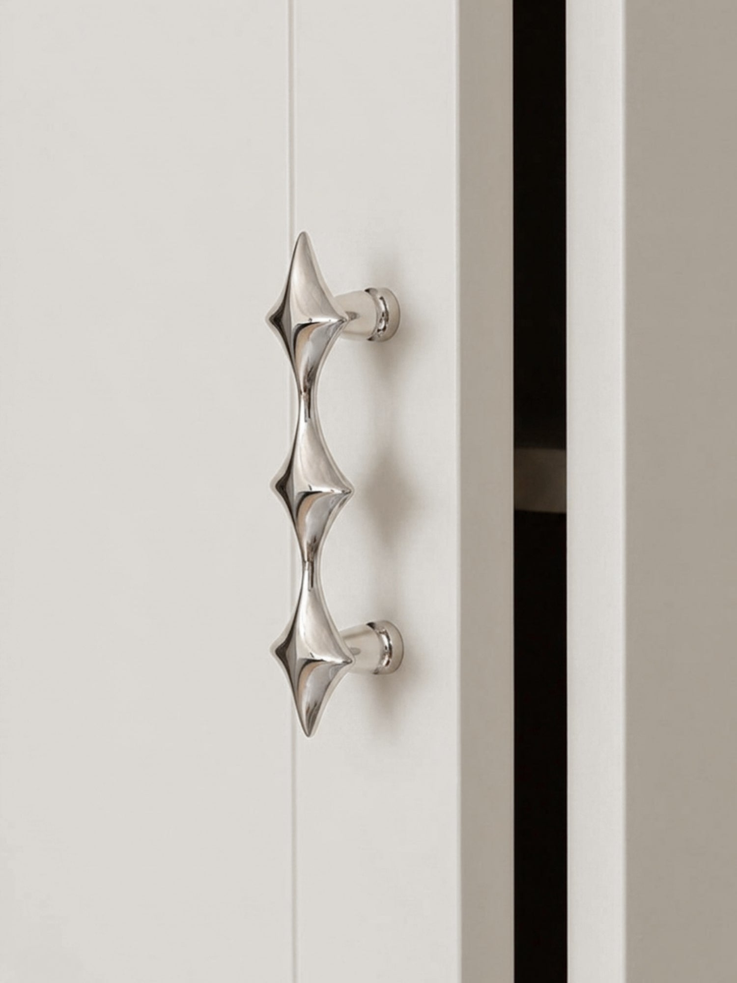 Single polished chrome star cabinet pull on white door, close-up side view