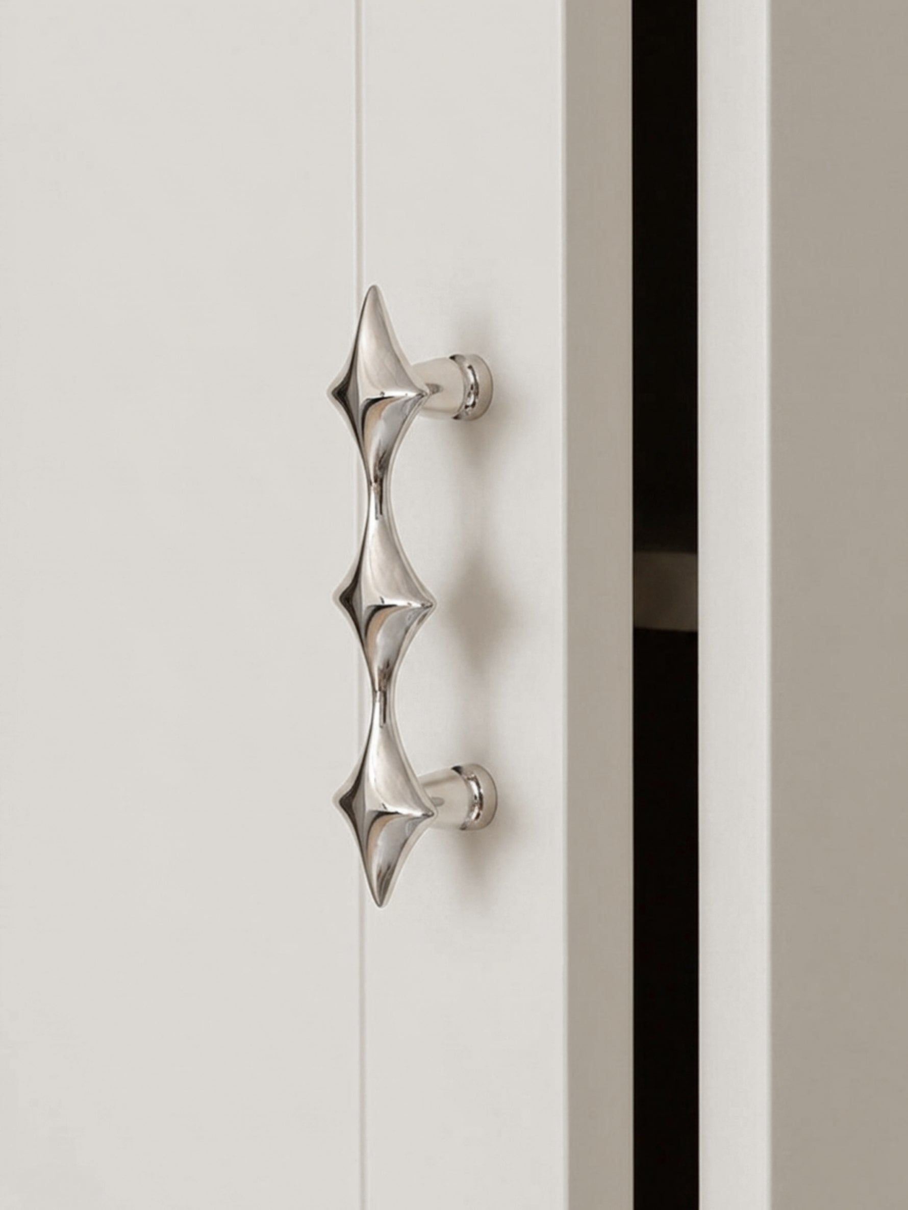 Single polished chrome star cabinet pull on white door, close-up side view