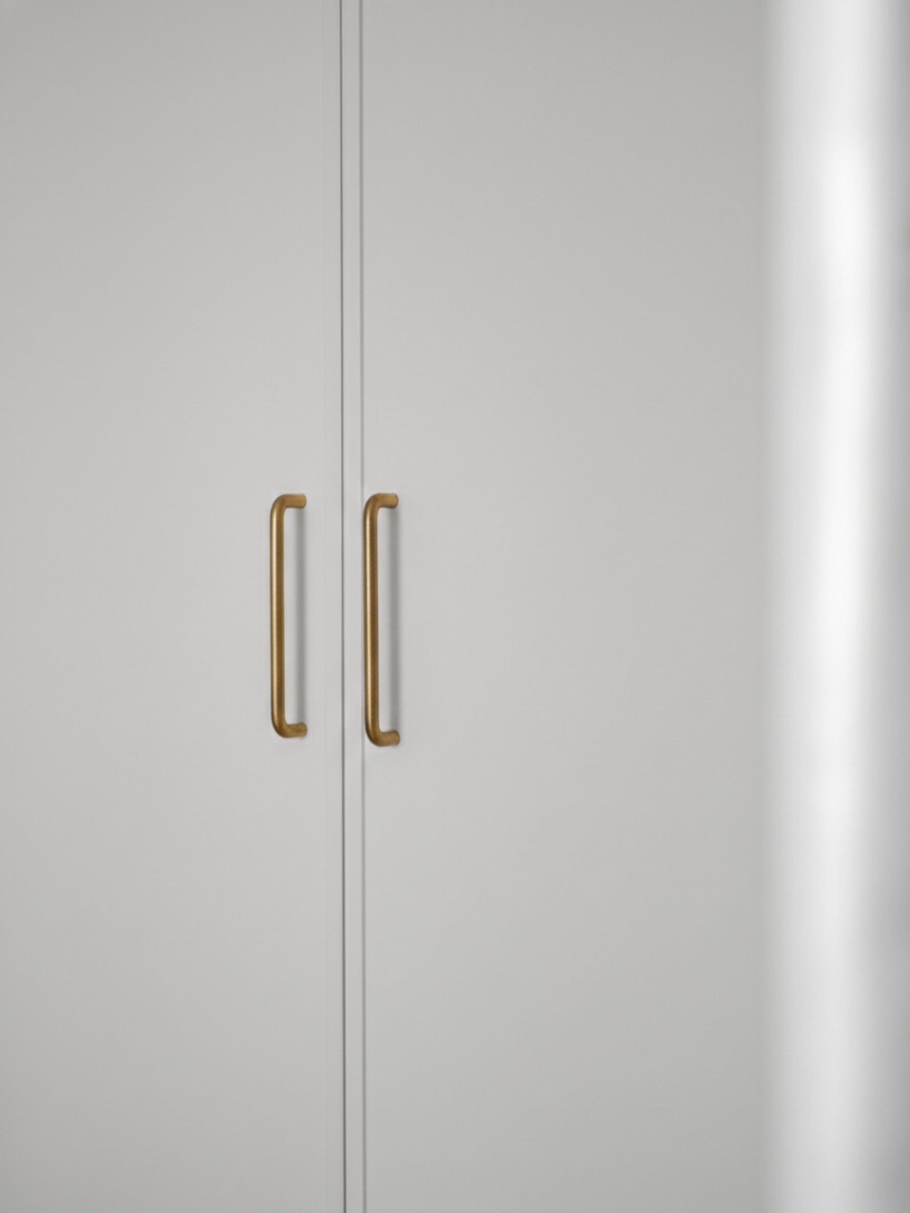 Close-up of a light gray cabinet with brushed brass handles on a white background