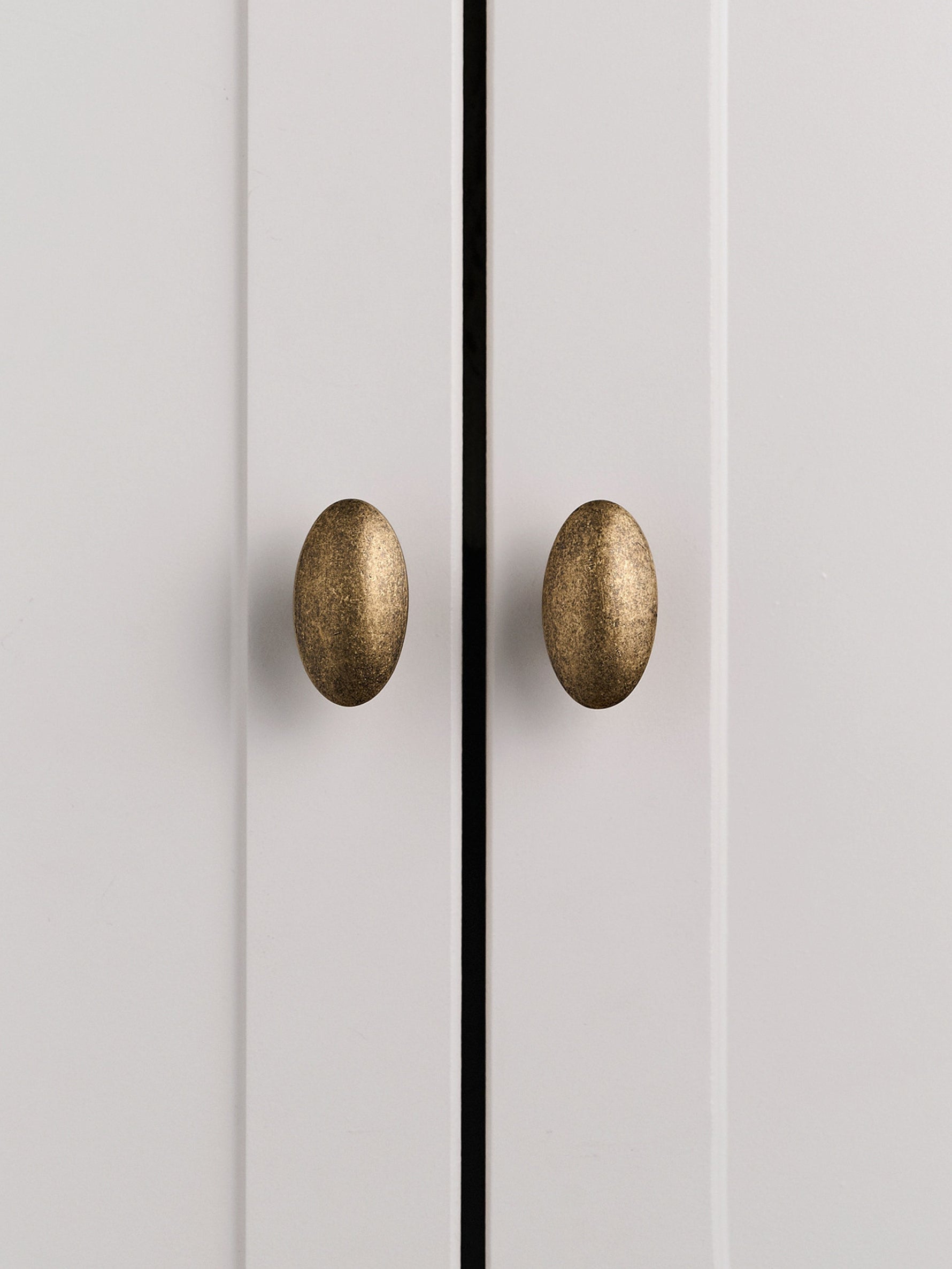 Two antique brass oval knobs on grey cabinet doors, front view