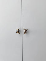 Two polished chrome wave star knobs mounted on light grey cabinet doors